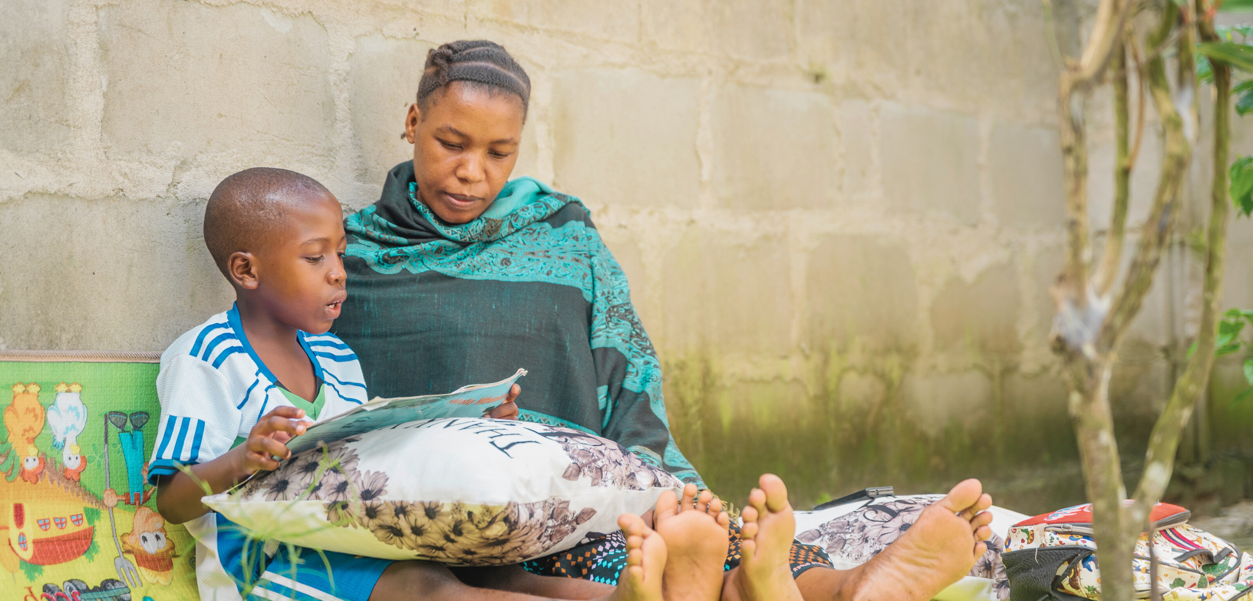 International Literacy Day, a mother reads with her son outside their home in Tanzania